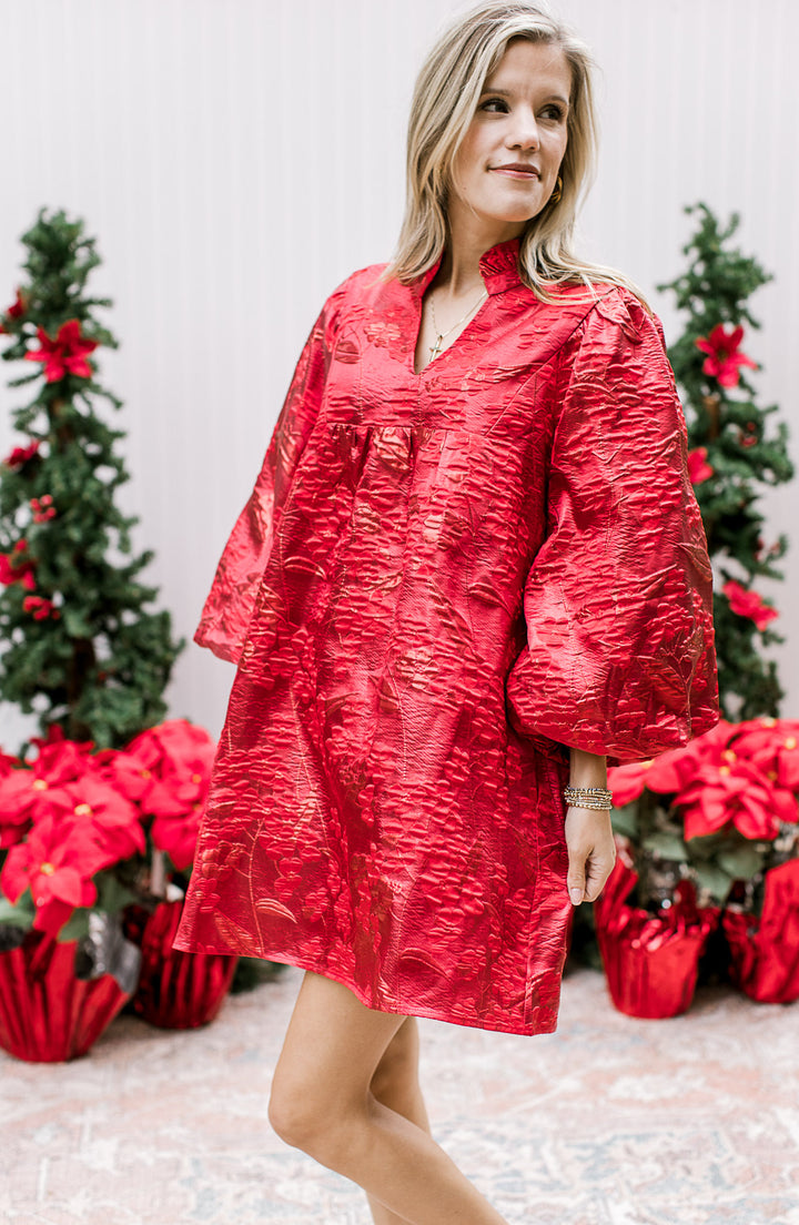 Model wearing a bright red dress with embossed floral shimmer, mock v-neck and bubble ¾ sleeves. 