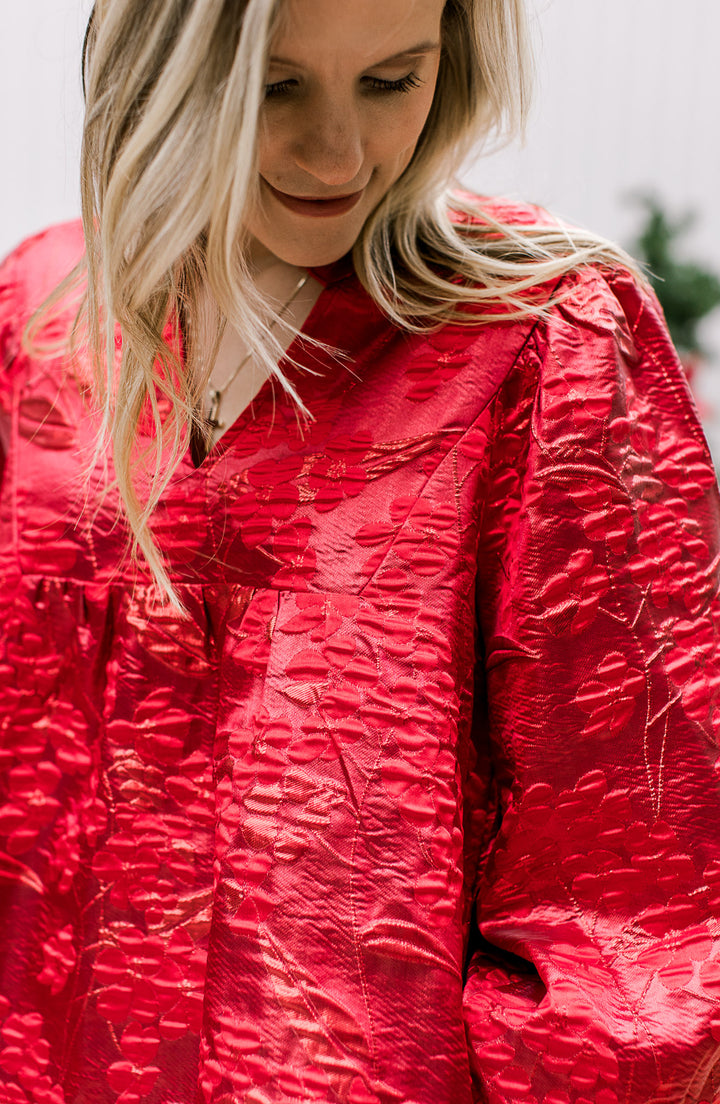 Close up of embossed floral shimmer on a bright red dress with a v-neck and bubble 3/4 sleeves. 