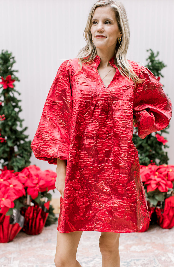 Model wearing an above the knee bright red dress with embossed floral shimmer and bubble sleeves.