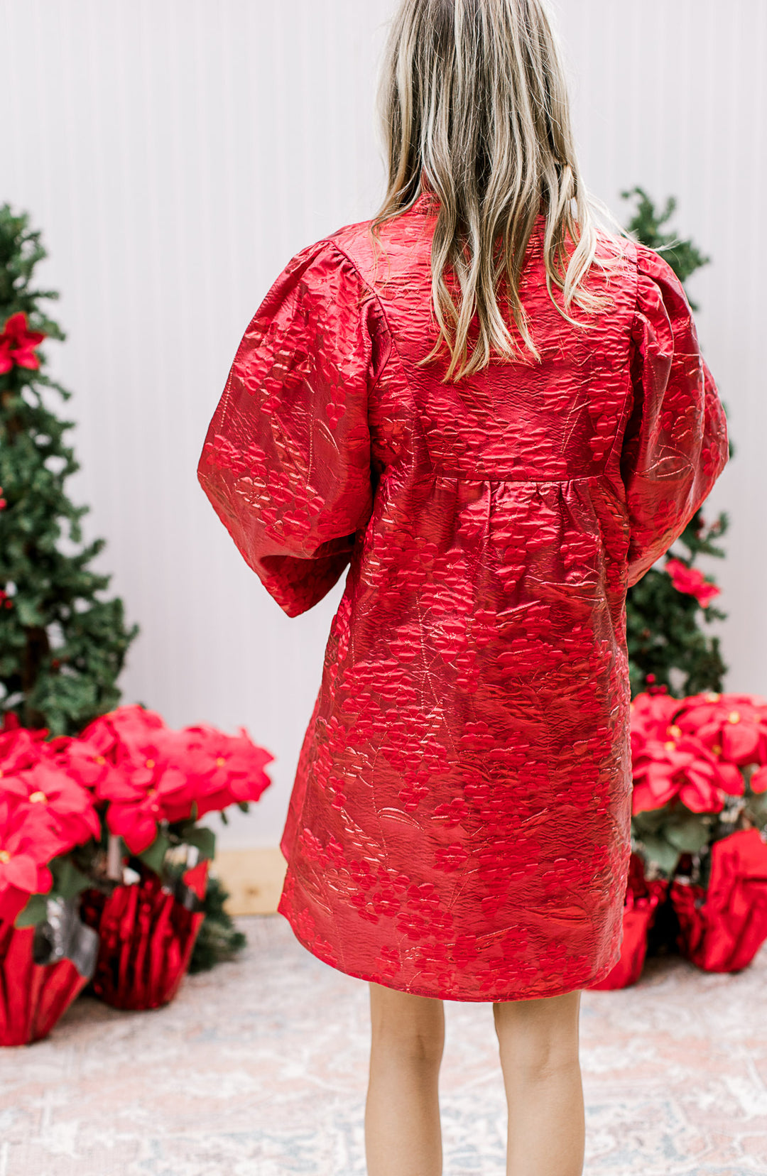Back view of Model wearing a bright red dress with embossed floral shimmer  and bubble ¾ sleeves. 