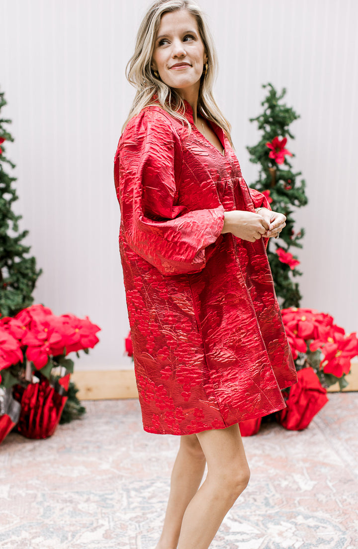 Model wearing a bright red dress with embossed floral shimmer, pockets and bubble ¾ sleeves. 