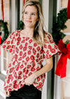Model wearing a cream top with red poppy’s, a brocade fabric, short sleeves and a high square neck. 