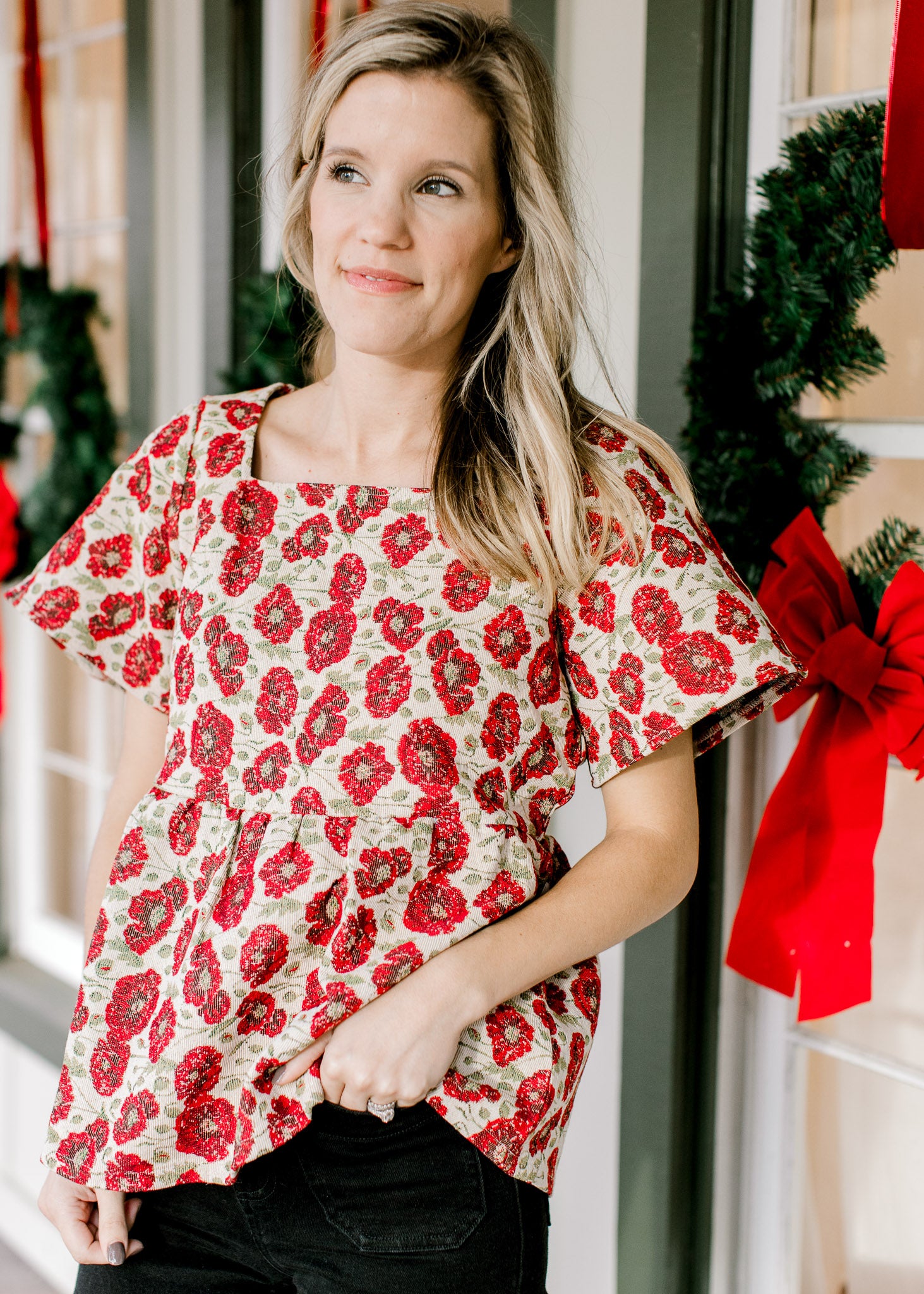 Model wearing a cream top with red poppy’s, a brocade fabric, short sleeves and a high square neck. 