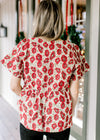 Back view of Model wearing a cream top with red poppy’s, short sleeves and a high square neck. 