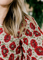 Close up of red poppy’s and green accents on a cream top with a brocade fabric and short sleeves. 