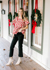 Model wearing black jeans and booties with a cream top with red poppy’s and a high square neck.