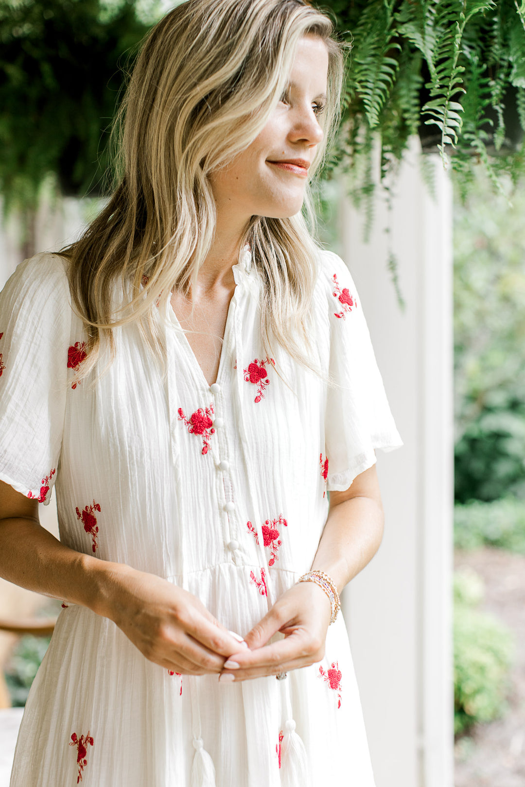 Close up of v-neck with tie and buttons down bodice of a white maxi with red flowers. 