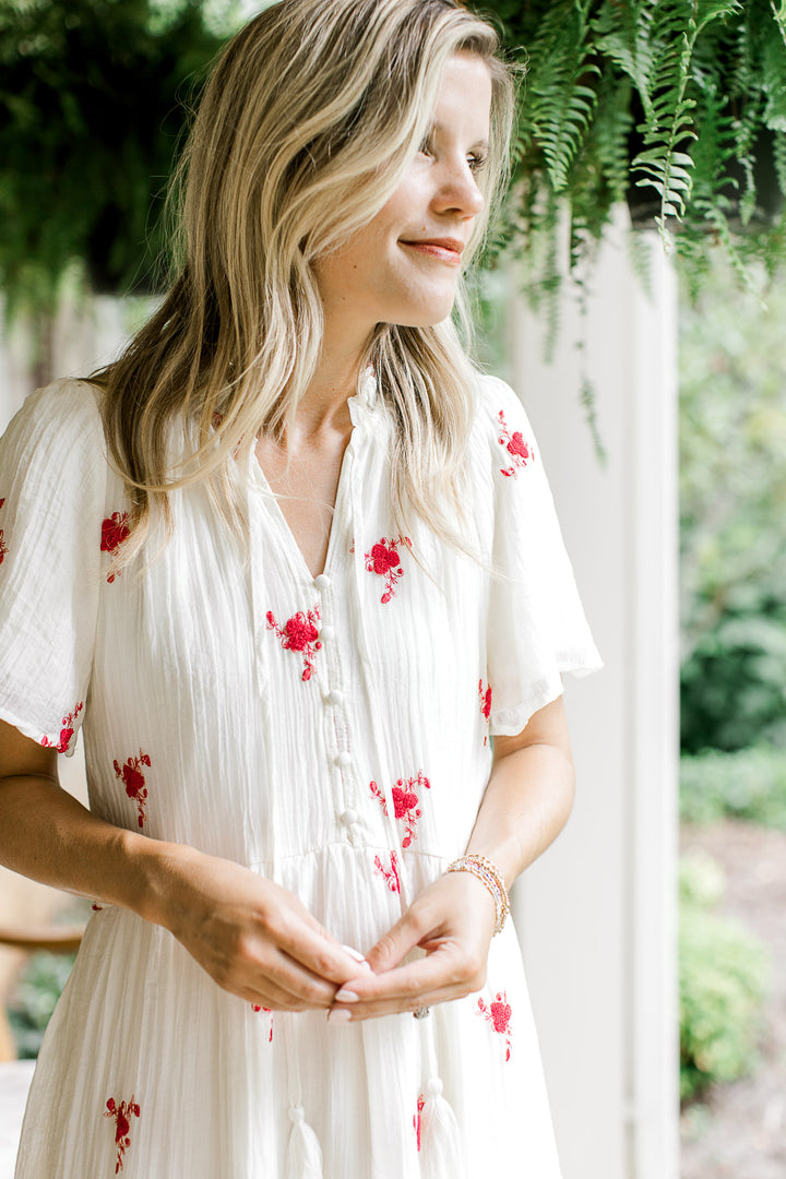 Close up of v-neck with tie and buttons down bodice of a white maxi with red flowers. 