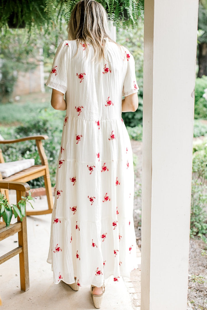 Back view of Model wearing a white maxi with red flowers, short sleeves and a v-neck. 