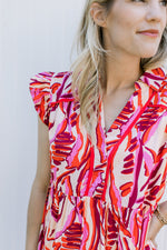 Close up of a cream above the knee dress with a red and pink floral design and ruffle cap sleeves. 