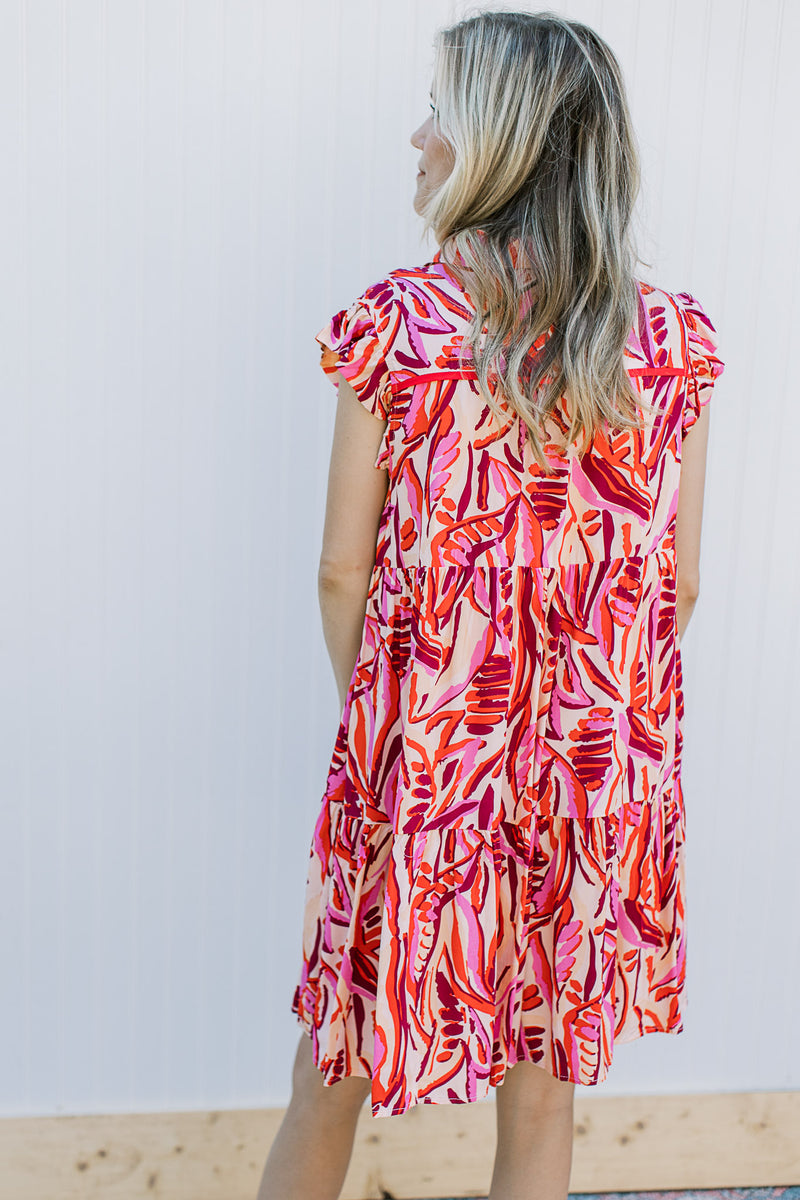 Back view of a model wearing a cream dress with a red and pink floral pattern. 