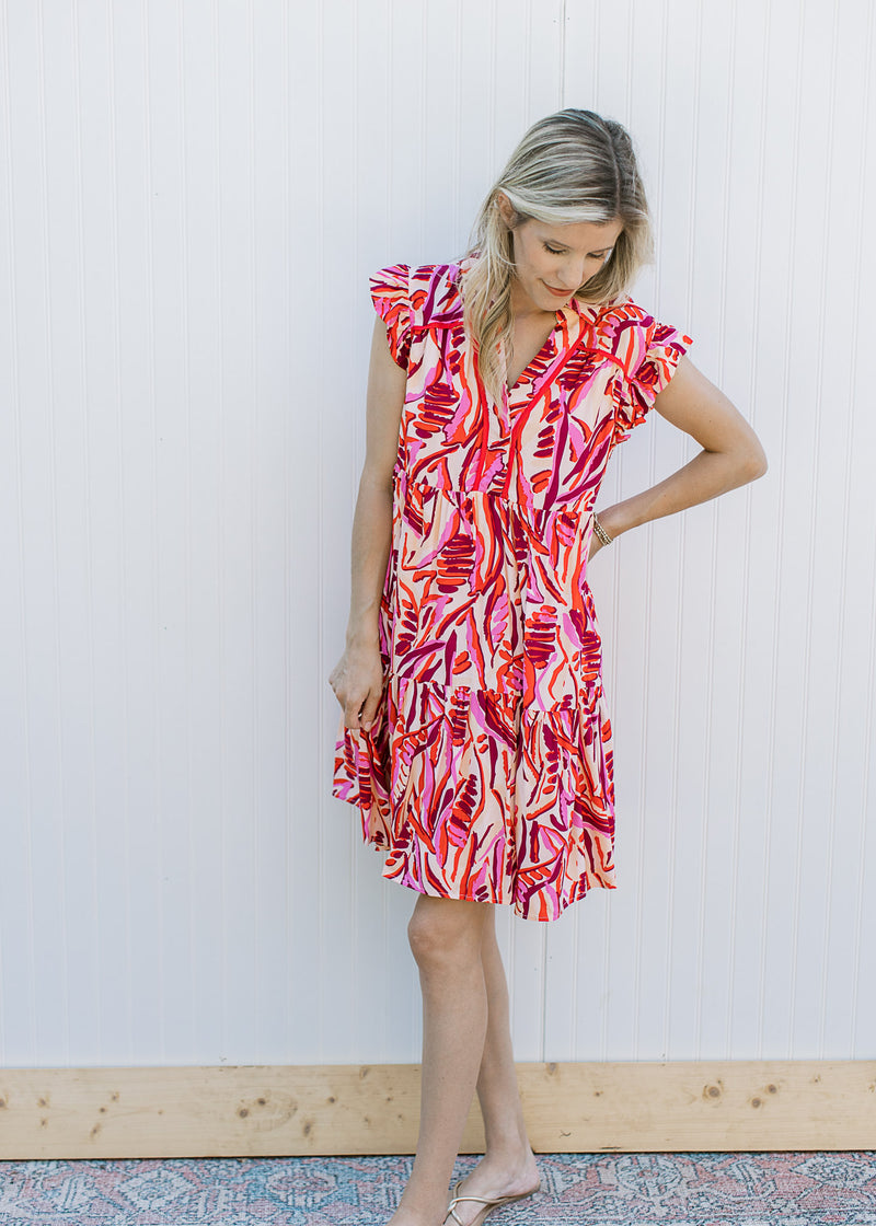 Model wearing a cream dress with a red and pink pattern, cap sleeves and a v-neck.