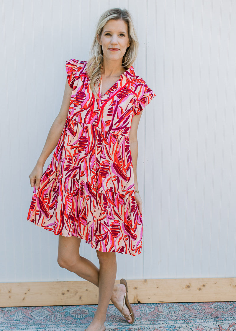 Model wearing sandals with a cream dress with a red and pink pattern, cap sleeves and a v-neck.