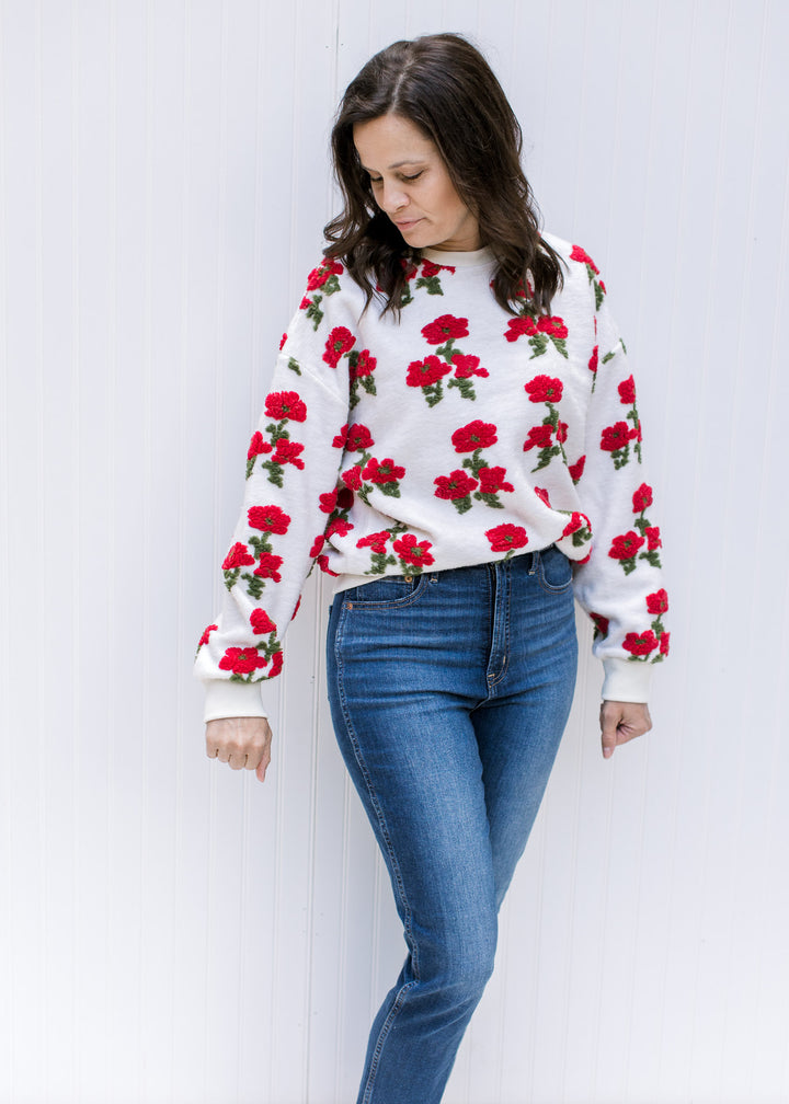 Model wearing an ivory long sleeve sweater with textured red poppies and ribbed neck, hem and cuff.