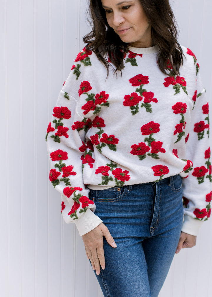 Model wearing an ivory sweater with red poppies, long sleeves, round neck and polyester material.