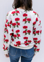 Back view of Model wearing an ivory sweater with textured red poppies, long sleeves and round neck. 