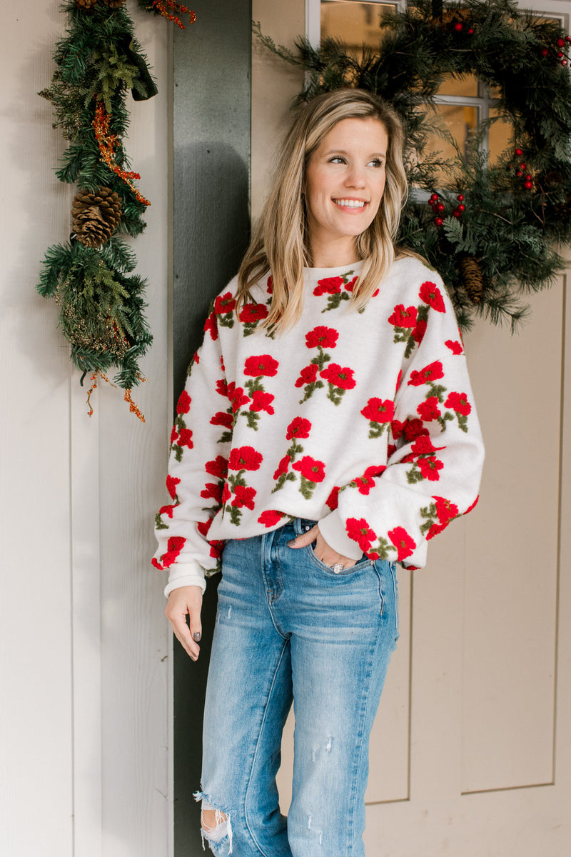 Model wearing an ivory sweater with textured red poppies, long sleeves and round neckline. 