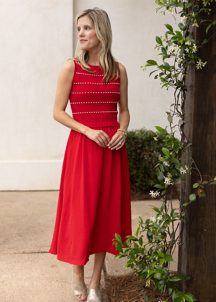 Model wearing heels and a red sleeveless midi with white stripes, smocked bodice and attached skirt.