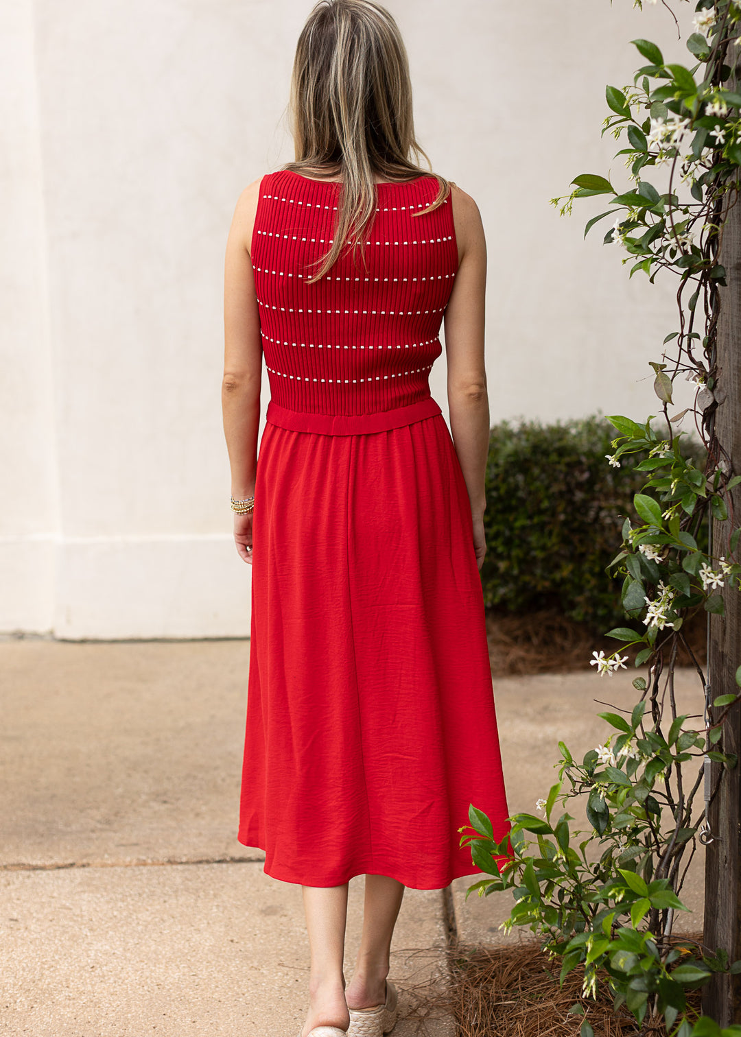 Back view of Model wearing a red sweater with thin white stripes, smocked bodice and attached skirt.
