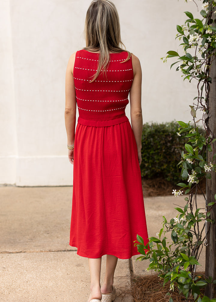 Back view of Model wearing a red sweater with thin white stripes, smocked bodice and attached skirt.