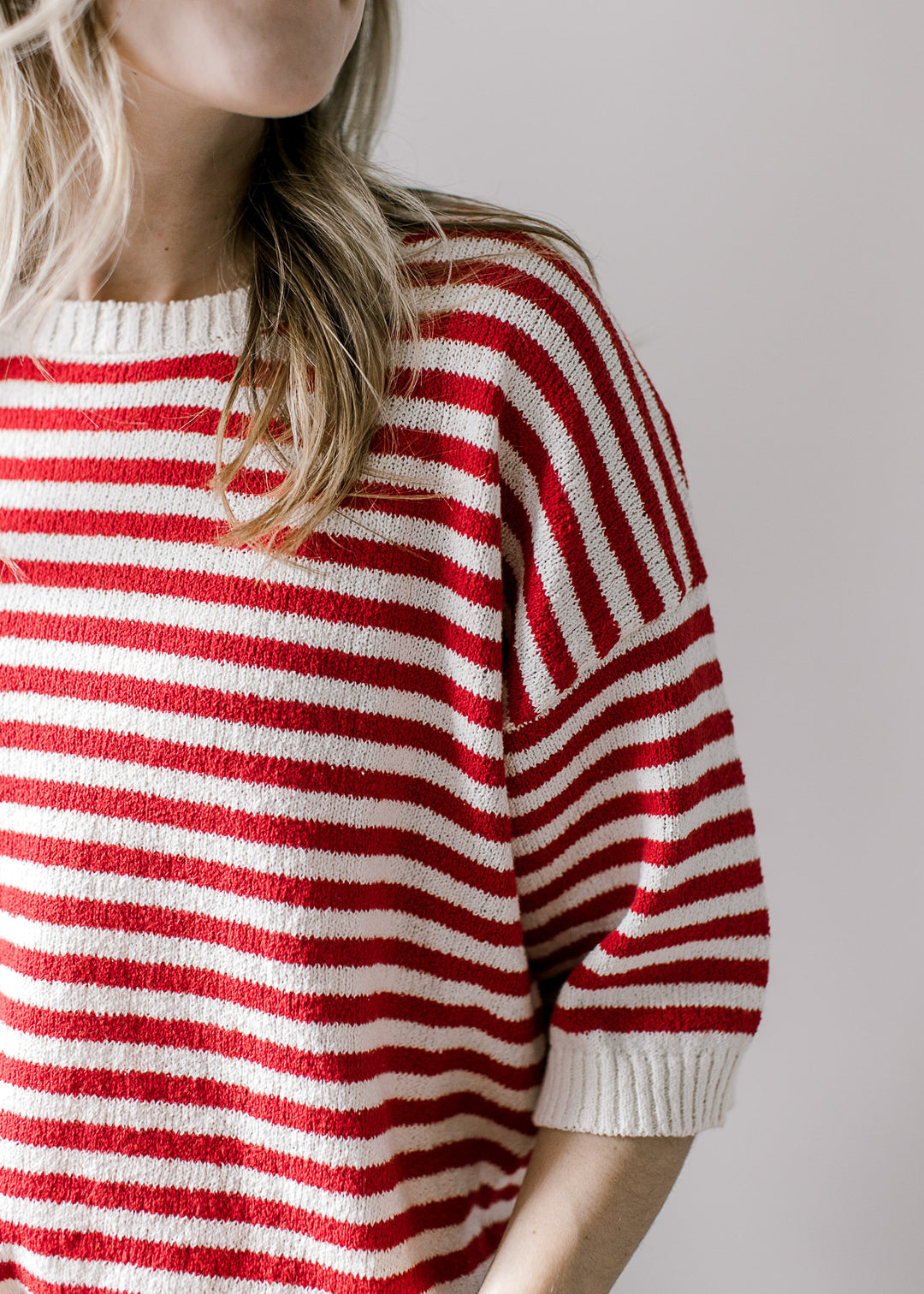 Close up of cream ribbing at neck and cuff of a red and white striped short sleeve sweater. 