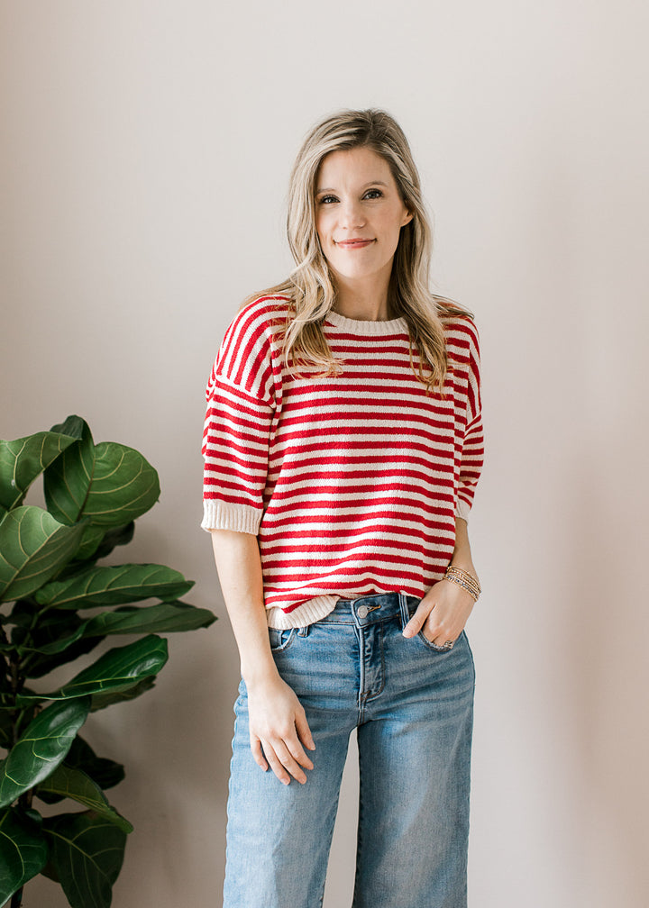 Model wearing jeans and a red and white striped sweater with short sleeves and button back. 