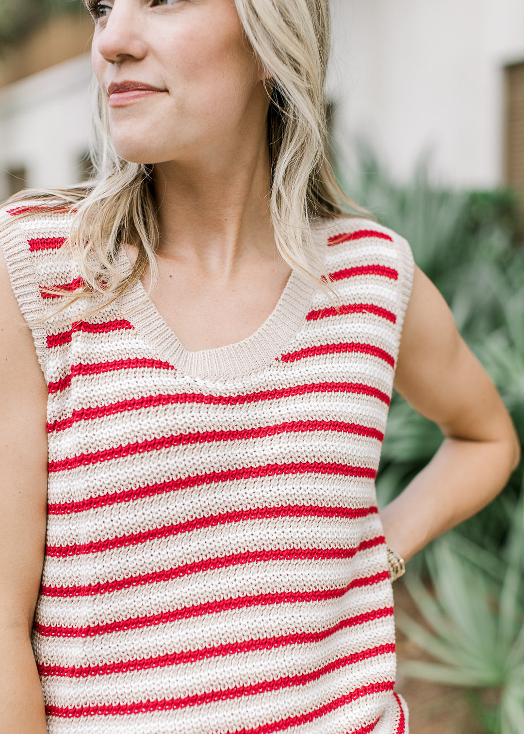 Model wearing a sleeveless red, cream, and white striped top with a knit material and round neck.