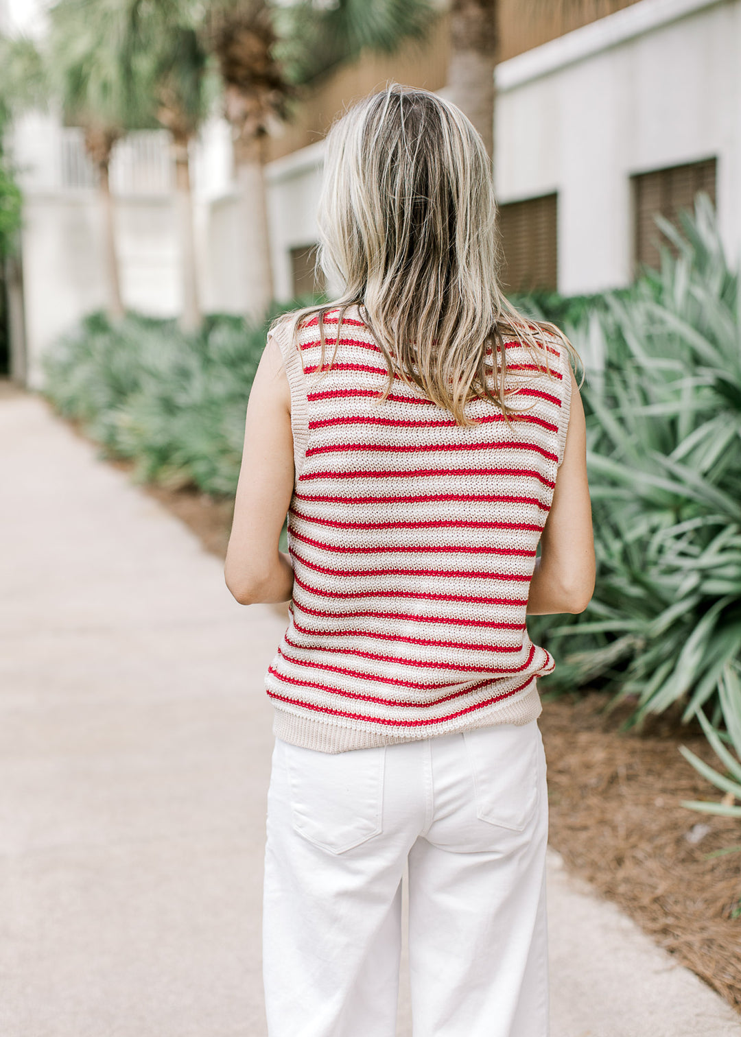 Back view of Model wearing a sleeveless red, cream, and white striped top with a knit material.