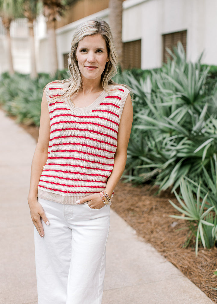 Model wearing white pants and a sleeveless red, cream, and white striped knit top. 