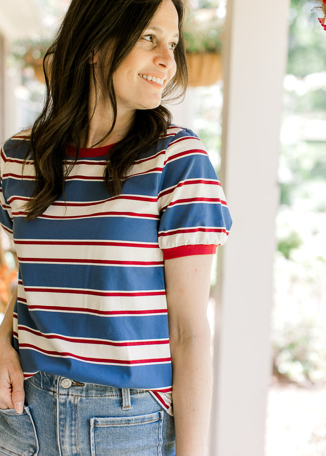 Model wearing a red, cream, and blue striped tee with short sleeves and a round neckline. 