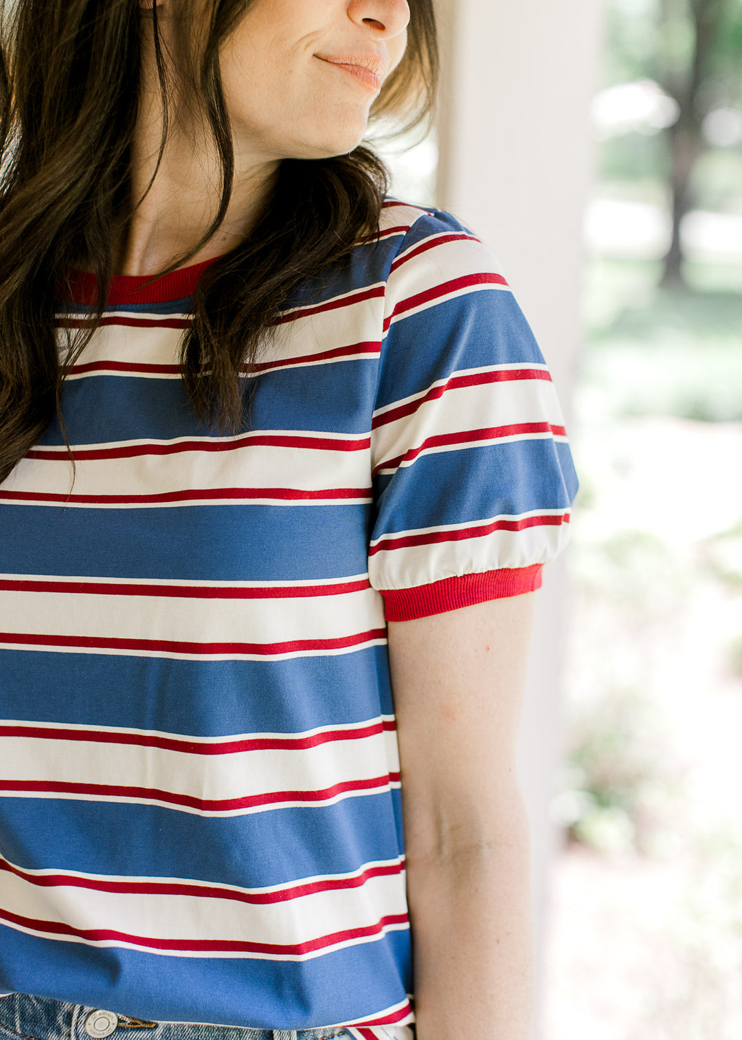 Close up of deep red cuff on short sleeve and round neckline of a red, cream and blue striped top.