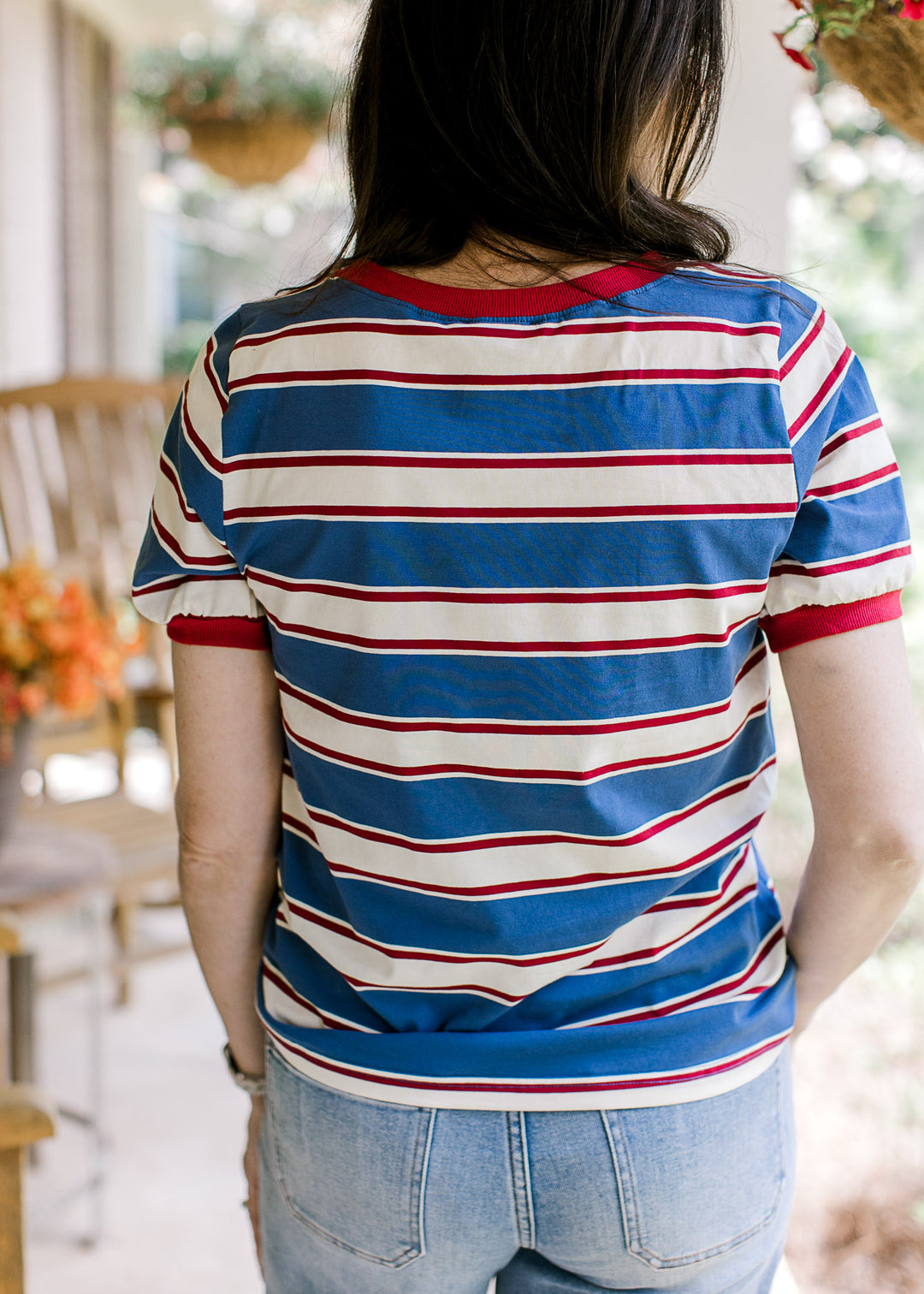 Back view of Model wearing a red, cream, and blue striped tee with short sleeves and a round neck.
