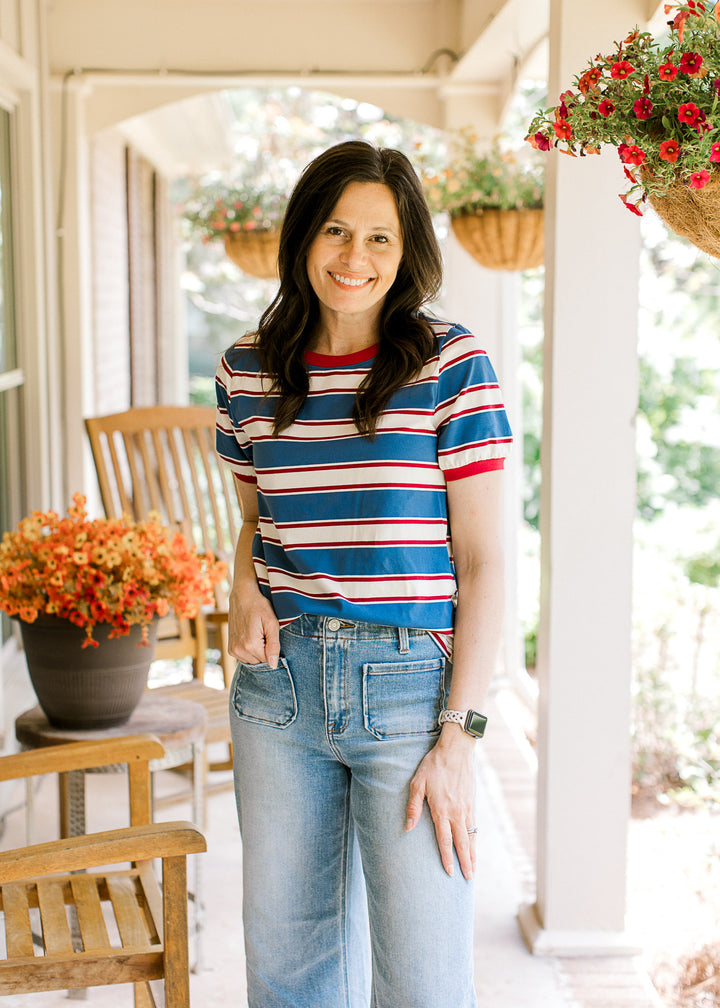 Model wearing jeans and a red, cream, and blue striped tee with short sleeves and a round neckline.