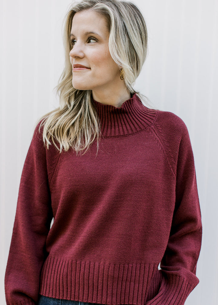 Model wearing a deep burgundy knit with a mock neckline, long sleeves and a slightly cropped fit.