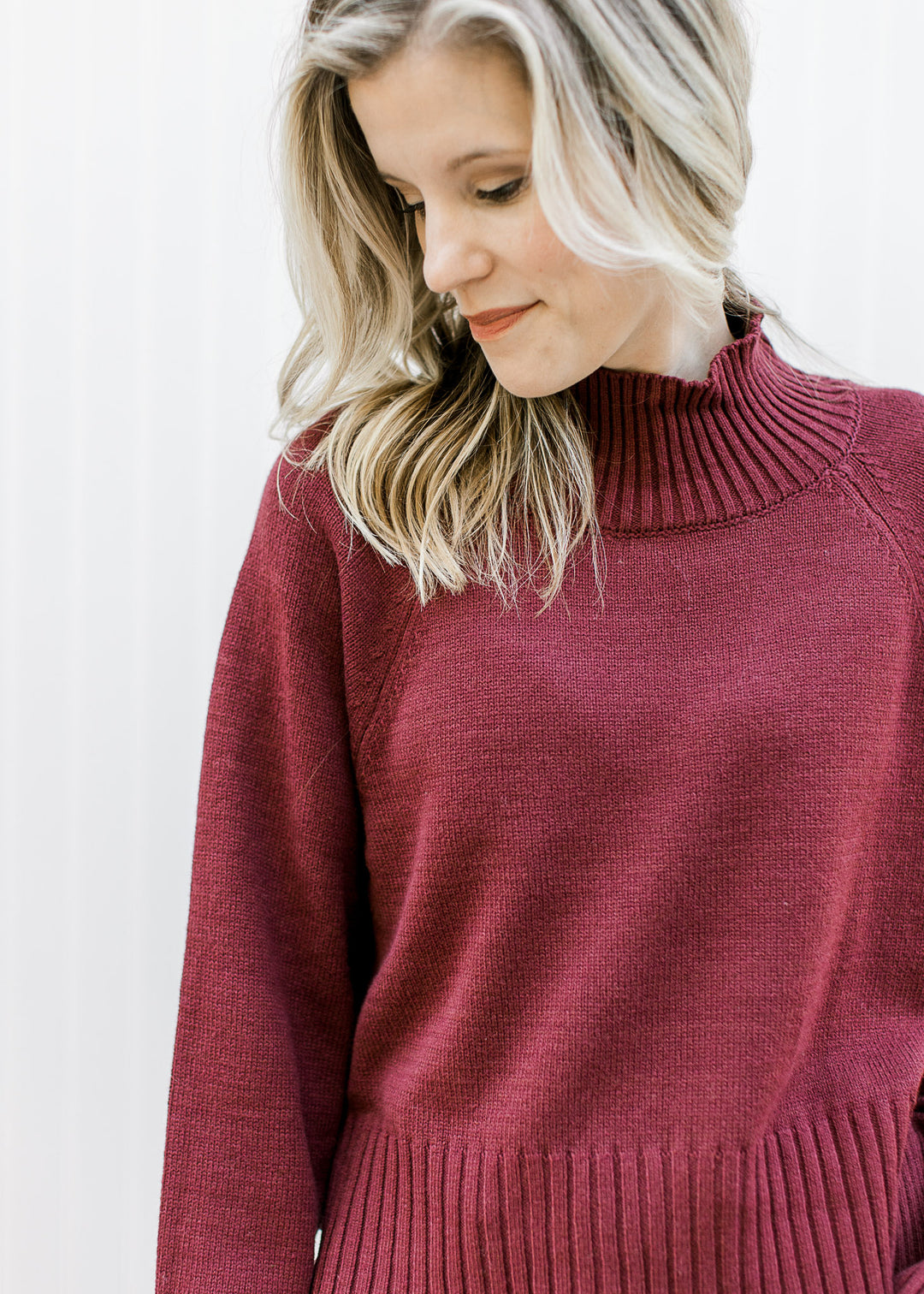 Model wearing a deep burgundy long sleeve sweater with ribbed mocked neck, hem and cuff. 