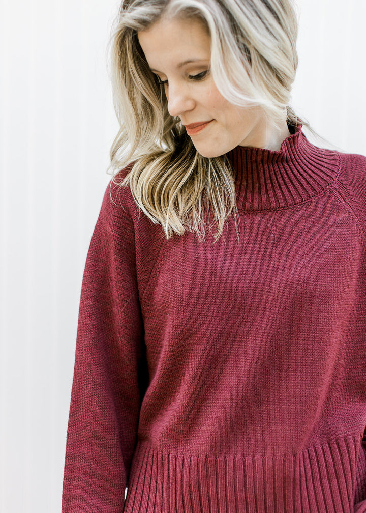 Model wearing a deep burgundy long sleeve sweater with ribbed mocked neck, hem and cuff. 