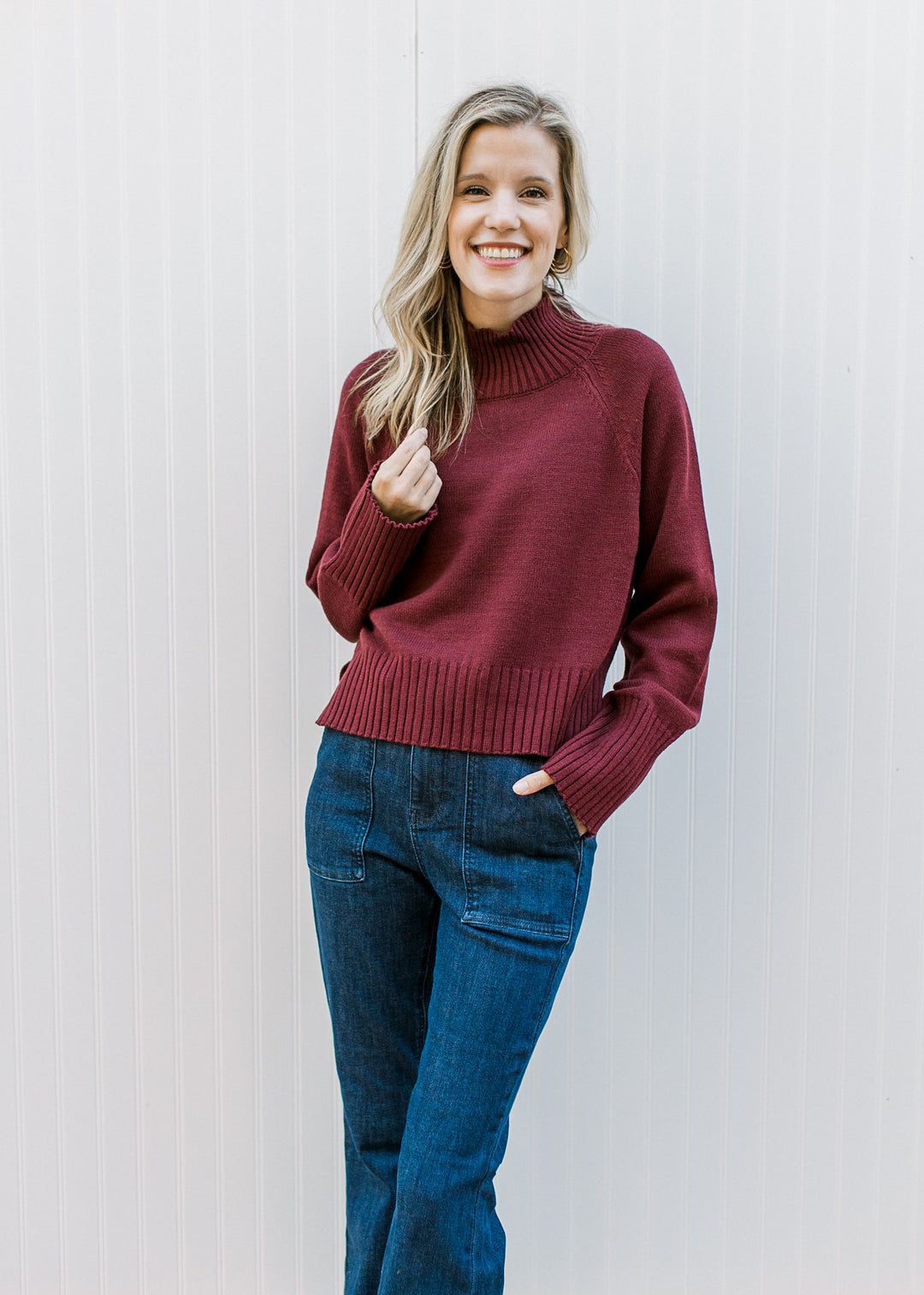 Model wearing jeans and a burgundy knit with a mock neck, long sleeves and a slightly cropped fit.