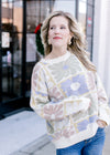 Model wearing a cream sweater with a graphic floral pattern, long sleeves and a round neck. 