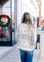 Back view of Model wearing a cream sweater with a graphic floral pattern and long sleeves.