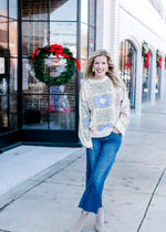 Model wearing jeans, booties and a cream sweater with a graphic floral pattern and long sleeves. 