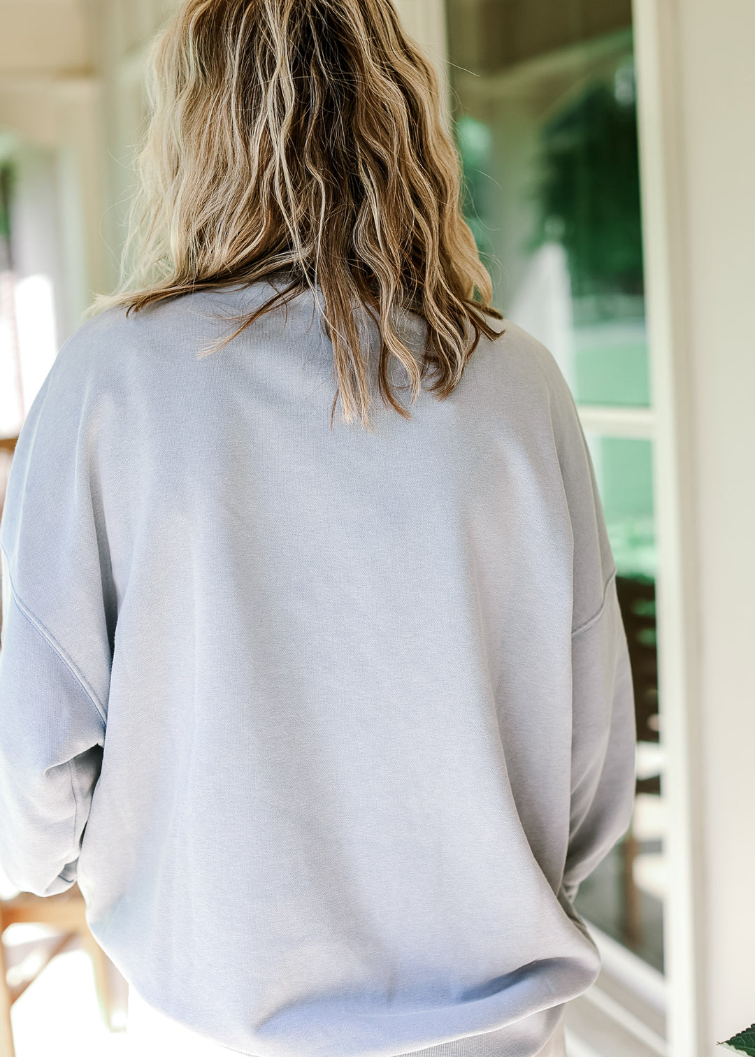 Back view of model wearing a pale blue lightweight sweatshirt with mock neckline and long sleeves.