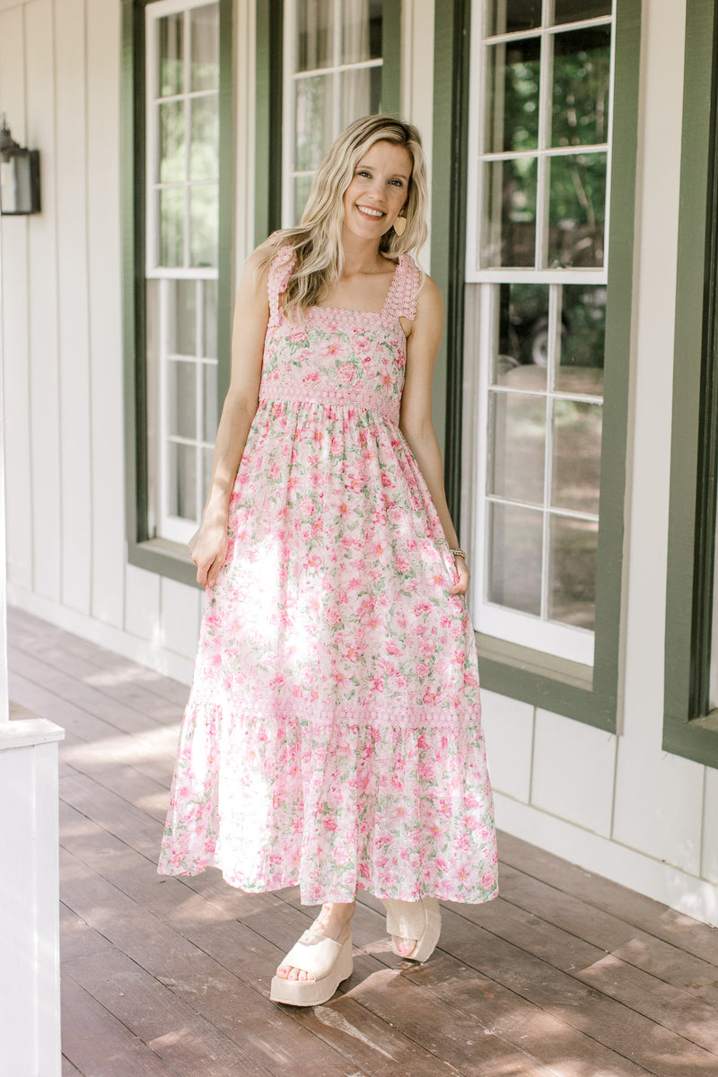 Model wearing a pink midi with pink and green flowers, lace detail and a polyester material. 
