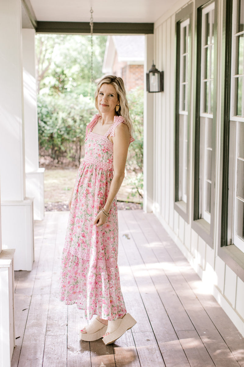 Model wearing a pink fully lined dress with pink and green flowers and tie spaghetti straps.