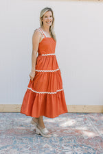 Model wearing wedges with a rust dress with ric rac detail, tank straps and a square neck. 