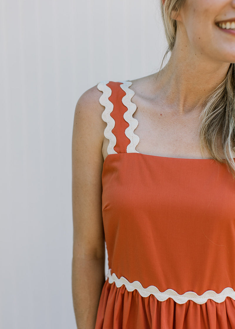 Close up of tank strap with ric rac detail in cream on a rust dress with a square neck. 