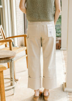 Back view of Model wearing light khaki cargo jeans with high waist and wide legs with large cuff.