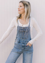 Model wearing light wash overalls with adjustable back tie and a cropped wide leg length.