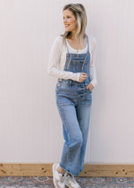 Model wearing sneakers and light wash overalls with adjustable tie and a cropped wide leg length.