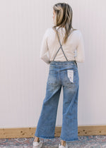 Back view of Model wearing light wash overalls with adjustable tie and a cropped wide leg length.