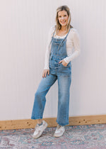 Model wearing a white top and light wash overalls with adjustable tie and cropped wide leg length.